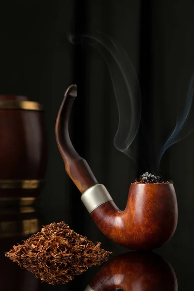 LIt Wooden Elegant Brown Tobacco pipe with tobacco and tobacco wooden containers in dark background. Unhealthy habit. This addiction and its pleasure is considered elegant for some yet bad for smokers.