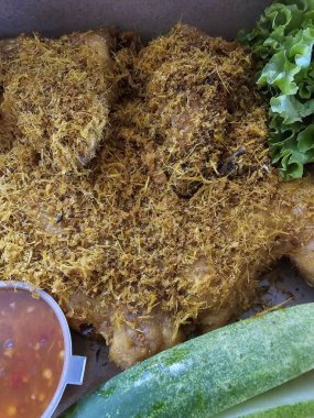 Mükemmelliğin tadını çıkar: Baharatlı hindistan cevizi gevreğiyle süslenmiş tam kızarmış tavuk, yanında salatalık dilimleri, marul ve ateşli sambal..