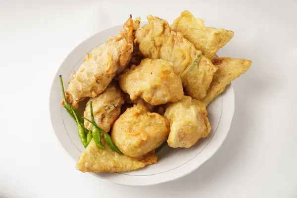 A plate of assorted fried snacks including stuffed tofu, tempeh, and fritters served with bird\'s eye chili. Captured against a white background. Popular for breaking fast and snacking.