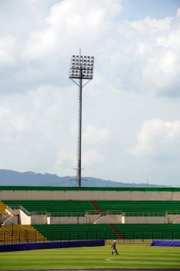 Bir bahçıvan, renkli seyirci koltuklarıyla süslenmiş canlı bir futbol stadyumundaki yemyeşil çimlerle ilgilenir.