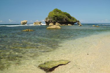 Gunungkidul 'da sakin bir sahil sahnesi. Beyaz kumlar, berrak sular ve yemyeşil sularla süslenmiş açık deniz kayaları.