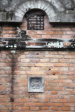 Kırmızı tuğladan yapılmış, karmaşık şekillerde şekillenmiş çimento süslemeleriyle süslenmiş, odak noktası olarak görev yapan ve geçmişin zanaatkarlığını gösteren bir duvar..