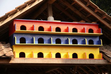 Parlak kırmızı, mavi ve sarı boyalı çok katlı bir kuş evi fayanslı bir çatının altına yerleşmiş, çok sayıda kapısı olan, kuş kiracılara hazır..
