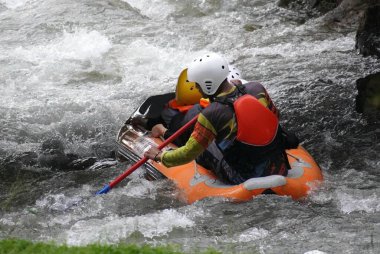 Bir grup insan hızla akan bir nehirde şişme bir botla rafting yapıyorlar, tam teçhizatlı güvenlik teçhizatlarıyla..