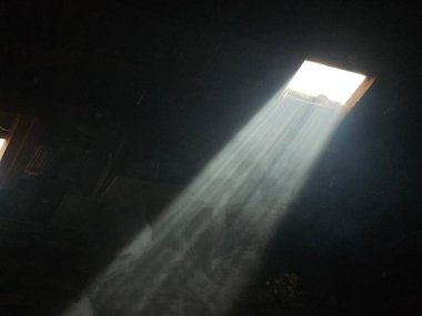 Güneş ışınları tek bir şeffaf çatı kiremitini delip geçer, odayı saran dumanla çarpıcı bir şekilde görünür hale gelir..