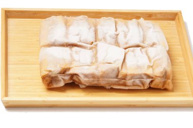 A vacuum-sealed plastic bag containing several frozen tofu bakso, square-shaped tofu with meatball filling tucked in the center, photographed on a wooden tray against a white background. clipart