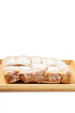 A vacuum-sealed plastic bag containing several frozen tofu bakso, square-shaped tofu with meatball filling tucked in the center, photographed on a wooden tray against a white background. clipart