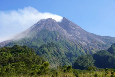 Yogyakarta, Endonezya 'daki Merapi Dağı, parlak mavi gökyüzüne karşı net bir şekilde görünen gri bir duman yayan aktif bir volkan.