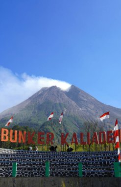 Yogyakarta, Endonezya - 25 Ağustos 2024: Bunker Kaliadem, Yogyakarta, Endonezya 'daki Merapi Dağı yakınlarında bir yeraltı sığınağı. Aktif volkan, gri zirvesi beyaz duman yayıyor.