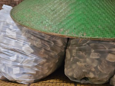 Kurutulmuş kasava dilimleri (Manihot esculenta) ile dolu iki büyük plastik torba, Gaplek olarak bilinir, pişirmeye hazırdır. Geleneksel bir bambu şapkası (pelerin) en üstte, kırsal bir dokunuş ekliyor.