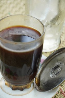 A glass of strong black coffee (Coffea arabica) with grounds, served on a saucer due to heat. Enjoy hot or with ice once cooled. A beloved drink among Indonesians. clipart