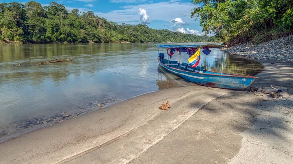stock image Touristic motor canoe with Ecuadorian flag stranded on a beach on the river shore of the Napo river in Ecuador on a sunny day with a beautiful blue sky
