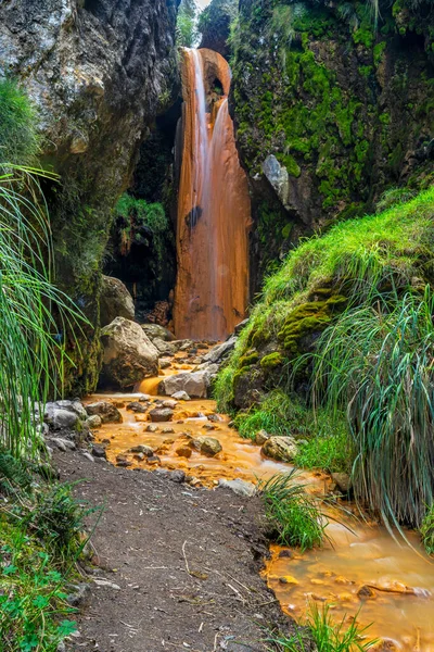 Vertical shot of the tropical golden waterfall located in the foothills of the volcano Illinizas Sur. Also called the red waterfall because the rocks turned red - orange due to the presence a large amount of volcanic minerals such as sulfur and iron.