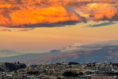Cayambe yanardağının hakim olduğu modern Quito şehrinin kuzeydoğusu ve bulutları alevlendiren bir günbatımı.