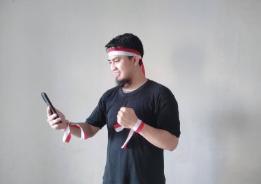 Cep telefonunu tutarken ve siyah tişört ve bantla mutlu bir Asyalı genç adam. Endonezya Bağımsızlık Günü konsepti.