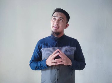 Olgun Asyalı adam mavi gömlek giyiyor. Düşünce jesti yapıyor. Gözleri yukarı bakıyor.