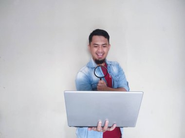 Olgun Asyalı adam, dizüstü bilgisayarına mutlu bir ifadeyle büyüteçten bakıyor.