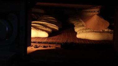 Endüstriyel taşıma bandı fırınından taze pişmiş ekmeğin altın kahverengi somunları geliyor.