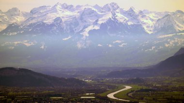 Avusturya ve İsviçre dağları karlı ve tepe tepe üzerinde küçük bir kasaba ve dolambaçlı bir nehir.