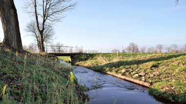 Nehir kışın ağaçlarla kaplı ve arka planda küçük bir köprü