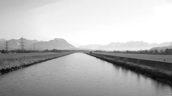 オーストリアとスイスの間の夏の日にはライン川があり ダムの道を自転車で進み 黒と白の背景に電柱と山があります — ストック写真