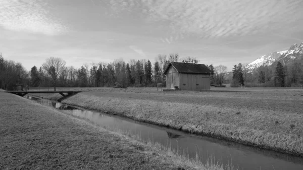黒と白の背景に橋や山と孤独な風景の中に木製の小屋の横に川 — ストック写真