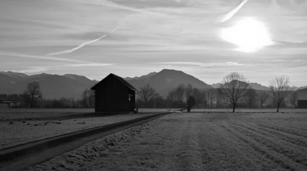 黒と白を背景に木々や山の風景のパスの横にある木造の小屋 — ストック写真