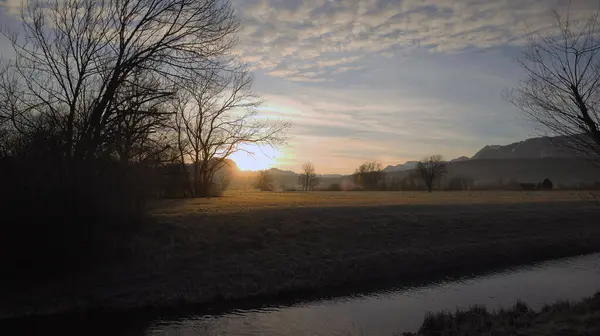 冬には隣に裸の木がある田舎の川の後ろの日の出 — ストック写真