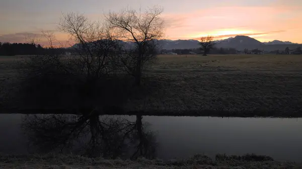 裸の木を反映して前景に川と山の後ろの日の出 — ストック写真