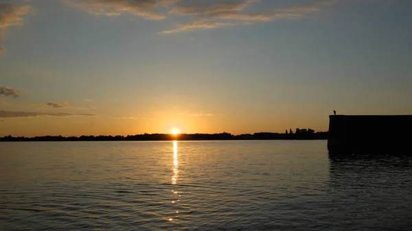 stock image Sunset behind horizon with reflection and glitter on lake and bird on wall