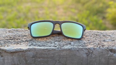 Beton bir yüzeyde plastik çerçeveli yeşil lensli güneş gözlükleri..