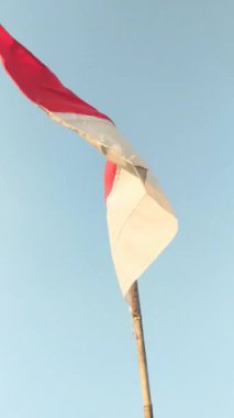 Endonezya bayrağı, kırmızı ve beyaz bir bicolor, açık mavi gökyüzüne karşı bambu direğinden dalgalanıyor. Bayrak rüzgarda dalgalanıyor.