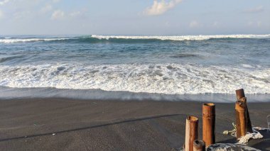 A vast ocean with large, rolling waves. The waves are crashing onto a sandy beach, creating white foam. The sky is blue with white clouds. In the distance, there are mountains or hills covered in fog. clipart