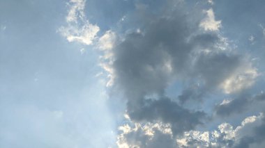 Yumuşak beyaz bulutları olan açık mavi bir gökyüzü. Bulutlar çeşitli şekil ve boyutlarda, bazıları da gölgelerle kaplı. Gökyüzü parlak ve havadar görünüyor.