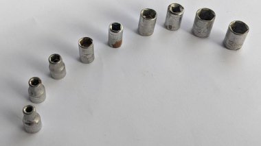 Beyaz arka planda çeşitli boyutlarda dokuz adet gümüş soket anahtarı var. Prizlerin farklı boyutlarda cıvata ve fındıklar için tasarlandıklarını gösteren altıgen açıklıkları var.