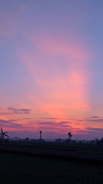 Nefes kesici pembe ve mor bir gün doğumu gökyüzünü boyar. İnce bulutlar tuval boyunca sürükleniyor, sükunet hissi yaratıyor. Sahne huzur ve merak uyandırıyor..