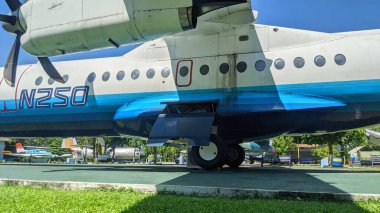 Bir IPTN N N-250 uçağının gövdesine ve pervanesine yakın çekim, ruhsatını gösteriyor, mavi alt ve iniş takımları, güneşli bir günde açık havada..