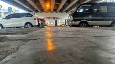 Alacakaranlıkta ya da gece bir caddenin alçak açılı görüntüsü. Arabalar üst geçidin altına park edilmiş. Sokak lambalarından gelen sıcak turuncu ışık ıslak betona yansıyor..