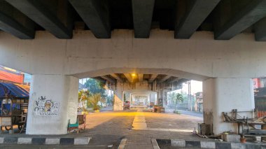 Şafakta veya alacakaranlıkta beton bir üstgeçidin altgeçidi, yolu aydınlatan tek bir ışık, grafitileri, park edilmiş arabaları ve uzak ağaçları ortaya çıkarıyor..