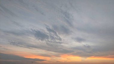 Ufukta koyu turuncu ve sarıdan açık mavi ve griye dönüşen geniş bir gökyüzü, dinamik bulut çizgileriyle dramatik bir gündoğumu sahnesi yaratıyor..