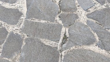 Düzensiz şekilleri ve pürüzlü dokuları olan kırsal gri kaldırım taşları, açık renkli havan topu ile ayarlanmış, dayanıklı ve doğal bir açık hava yüzeyi oluşturur...