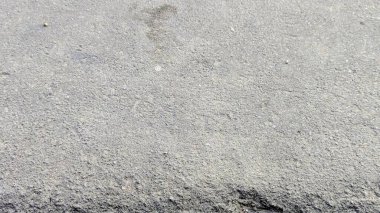 Kaba, gri asfalt ya da betondan oluşan detaylı bir yakın plan, doğal ışık altında kaba dokusunu ve granüler yüzeyini gösteriyor..