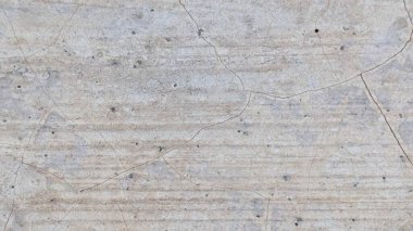 Yıpranmış, açık gri beton bir duvarın yakın çekimi. Yüzey ince çatlaklarla kaplı. Doku ince yatay çizgiler ve küçük koyu noktalar gösteriyor..