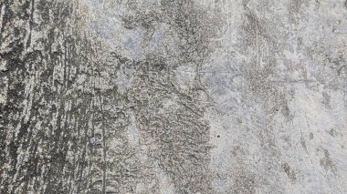 Beton bir yüzeyin yüksek açılı yakın çekimi. Sol taraf koyu ve pürüzlü, sağ taraftaki açık renkli, pürüzsüz kısma zıt, ince çatlaklar ve desenler gösteriyor..