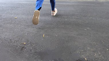 Bir insanın ayaklarının ve bacaklarının asfalt zeminde koşarken orta adım attığı dinamik ve düşük açılı bir çekim. Bir ayağı havada, hareket halinde..