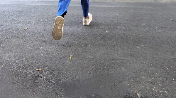Bir insanın ayaklarının ve bacaklarının asfalt zeminde koşarken orta adım attığı dinamik ve düşük açılı bir çekim. Bir ayağı havada, hareket halinde..