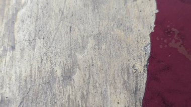 Dokulu yüzeyin iki kısma ayrılmış yakın çekimi. Sol tarafı çatlak, soluk beyaz bir duvar, sağ tarafı ise canlı, koyu kırmızı, kenarları soyulmuş ve hasarlı..