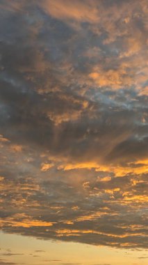 Dokulu bulutlarla dolu engin bir gökyüzünün dikey görüntüsü. Karanlık, karamsar gri ve mavi bulutlar güneşin doğuşundan gelen parlak, ateşli portakallarla iç içe geçerek güçlü ve soyut bir desen oluştururlar..
