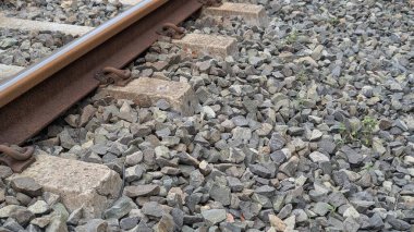 Demiryolu rayları, paslı metal raylara ve onu destekleyen taş safraya odaklanıyor. Kayaların ve betonun çeşitli tonları ve gri ve kahverengi renkleri açıkça görülebiliyor..