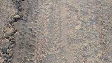 Sağında ince, tozlu toprak ve solunda çatlamış, daha büyük toprak kütleleri olan kuru bir zemin. Işık gölgeler oluşturur, düz olmayan yüzeyi aydınlatır..